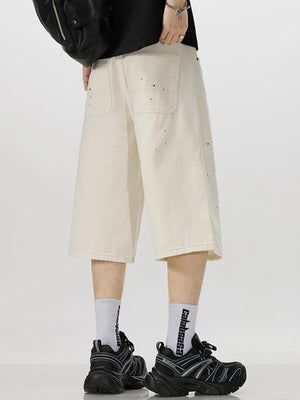 Cream cotton denim capris with artistic green splatter detail and wide leg cut.