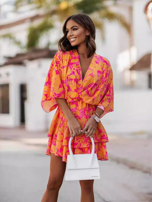 Tropical tiered mini dress in orange and hot pink floral print, with surplice neckline and short sleeves.