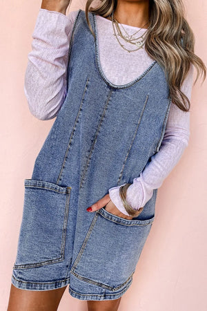 Acid wash denim romper with patch pockets and a v-neck, layered over a light purple long sleeve top.