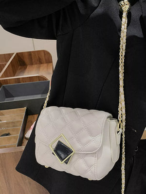 Elegant quilted crossbody bag in white with gold chain strap and geometric charm detail.