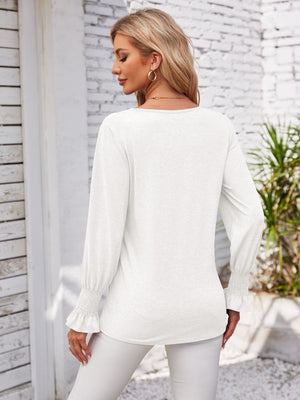 White blouson sleeve top with smocked cuffs and V-neck detail.