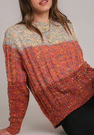 Ombre cable knit crewneck sweater in orange-red with flecks of color.