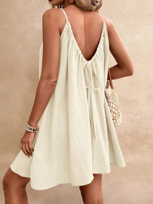 Beige spaghetti strap mini dress with back tie detail and textured fabric.