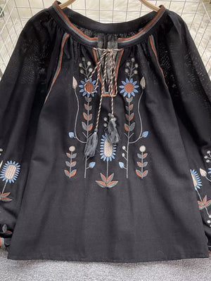 Black tie neck blouse with colorful floral embroidery and billowy sleeves.