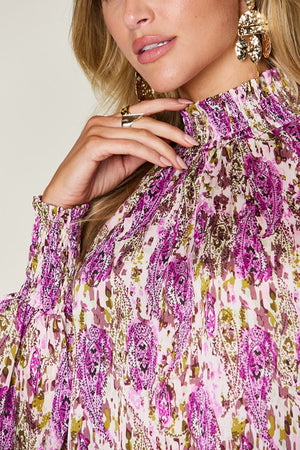 High neck abstract print blouse with smocked cuffs and collar in red-violet and white.