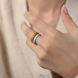 Gold chain link ring stacked with a light blue enamel band ring on a woman's finger.