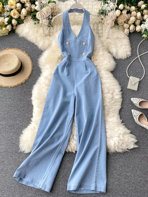 Light blue denim halter jumpsuit with wide legs and gold button detail.