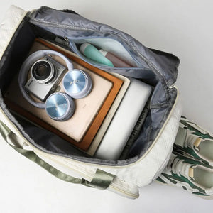 White quilted duffel bag with olive accents, open with camera, headphones, tablet, laptop and toiletries inside.