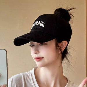 Black cotton visor hat with embroidered Colorado text, adjustable strap, and a bun hairstyle.