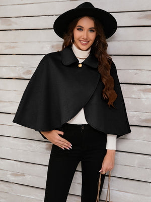 Black asymmetric cape jacket with button front and collar, styled with a hat and turtleneck.