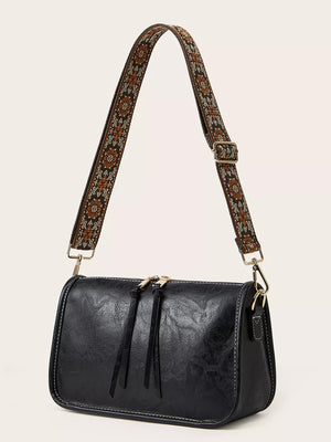 Black crossbody bag with adjustable patterned strap and tassel zipper pulls