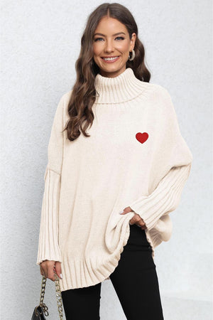 Beige batwing knit turtleneck sweater with red heart embroidery and ribbed sleeves.