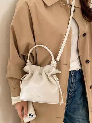 White pu leather cinch-top crossbody bag with knotted handle and drawstring closure.