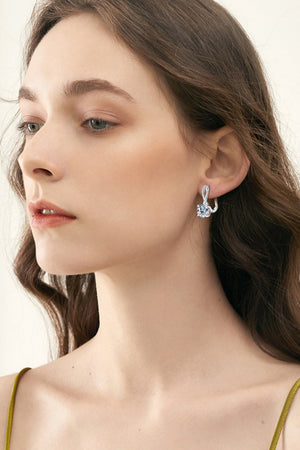 Silver crossover moissanite huggie earrings with a twisted detail and a round stone.