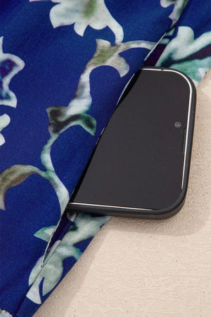 Vibrant floral maxi dress with frilled collar and buttoned front, showing a side pocket holding a smartphone.