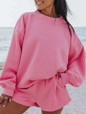 Pink crew neck sweatshirt and matching shorts lounge set on a beach.
