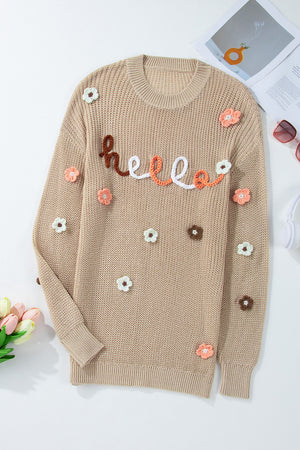 Khaki knit sweater with embroidered "hello" text and floral appliques.