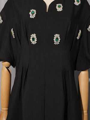 Black midi dress with puff sleeves and scattered rhinestone and emerald embellishments.