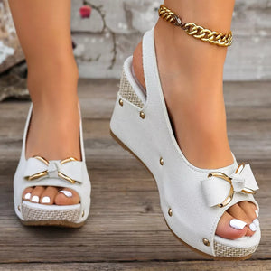 White peep toe wedge sandals with decorative bow detail and gold accents.