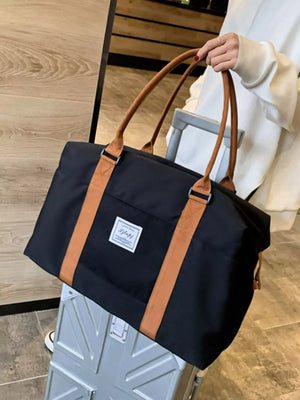 Large black Oxford cloth travel bag with contrast tan straps and handles.