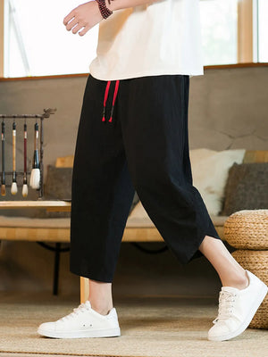Men's black cropped sweatpants with red drawstring detail and side slits.