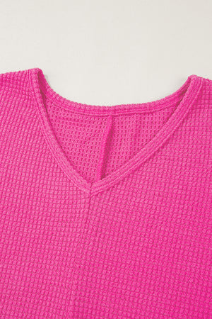 Hot pink waffle knit V-neck top with a slit hem detail.