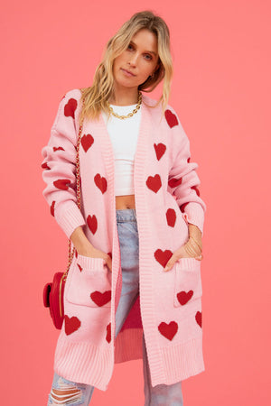 Blush pink longline knit cardigan with red heart pattern, featuring pockets and a relaxed fit.