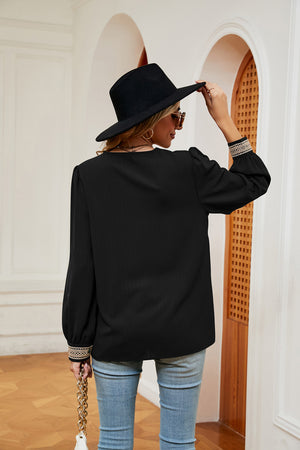 Black blouson top with embroidered trim on sleeves and V-neck.