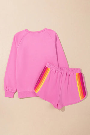 Fuchsia pink loungewear set with rainbow stripe detail on shorts and crewneck sweatshirt.