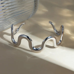 Sculptural silver cuff bracelet with a wavy, fluid design.