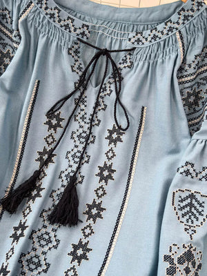 Light blue embroidered tie neck blouse with tassels and peasant sleeves.