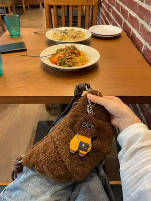 Brown plush crossbody bag with knot strap and dog charm accessory.