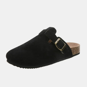 Black suede clog slides with adjustable buckle and cork sole.