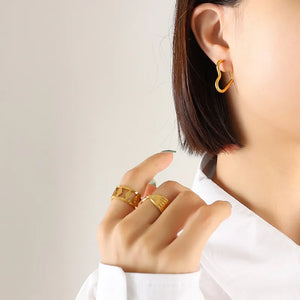 Gold heart huggie earrings and geometric rings on a woman's hand.