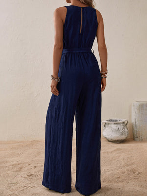 Navy textured wrap-front wide-leg jumpsuit with belted waist and sleeveless design.