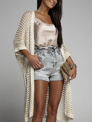 Cream open-knit duster cardigan with relaxed fit and open front, styled with a cami and denim shorts.