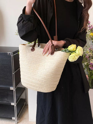 Natural straw woven large shoulder bag with brown leather straps, holding yellow flowers.