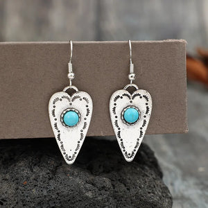 Silver heart-shaped dangle earrings with turquoise stones and tribal etched details.