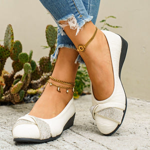 Beige slip-on wedge flats with rhinestone bow detail and textured fabric.