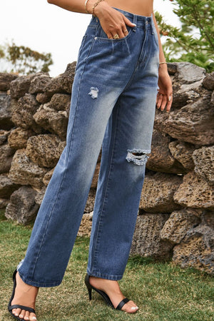Distressed wide-leg denim trousers in medium wash with ripped details and frayed hem.
