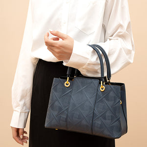 Elegant blue trapezoid tote handbag with geometric embossed pattern and gold hardware.