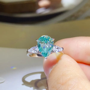 Silver ring with a large teal teardrop moissanite and two pear-cut side stones.