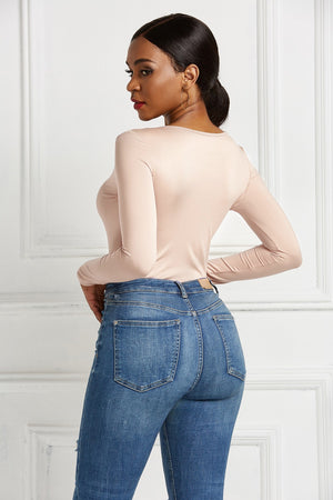 Beige long sleeve bodysuit with a plunging neckline and zip front, styled with denim jeans.