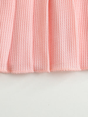 Pink waffle knit baby dress with a pleated hem.