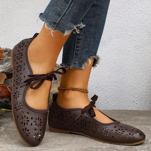 Brown floral cutout slip-on flats with tie detail and ankle chain styling.