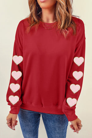 Deep red sweatshirt with pink heart appliqué details on the sleeves.