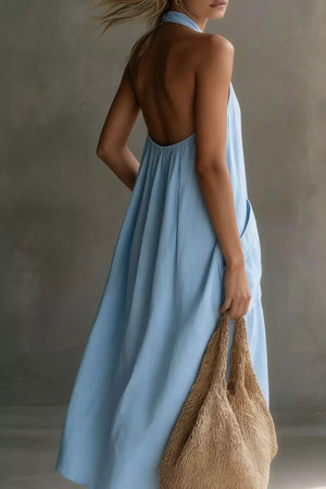 Light blue halter midi dress with pockets and an open back, shown with a straw bag.