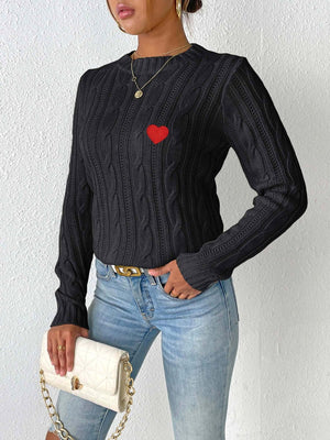 Black cable knit sweater with embroidered red heart detail.