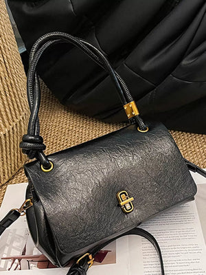 Black leather crossbody bag with twisted handle and gold clasp closure