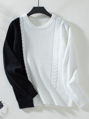 Colorblock cable knit sweater in black and white with textured stitch details.
